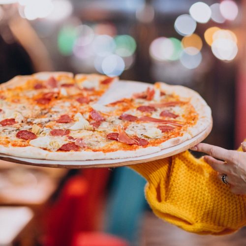 Waiter holding tasty salami pizza on a plate
